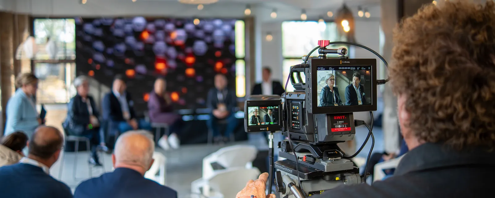 Camera monitor showing panel speakers, with the audience behind