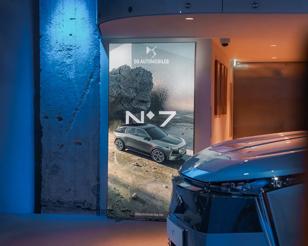 Car poster and the front of a car in a blue-lit showroom